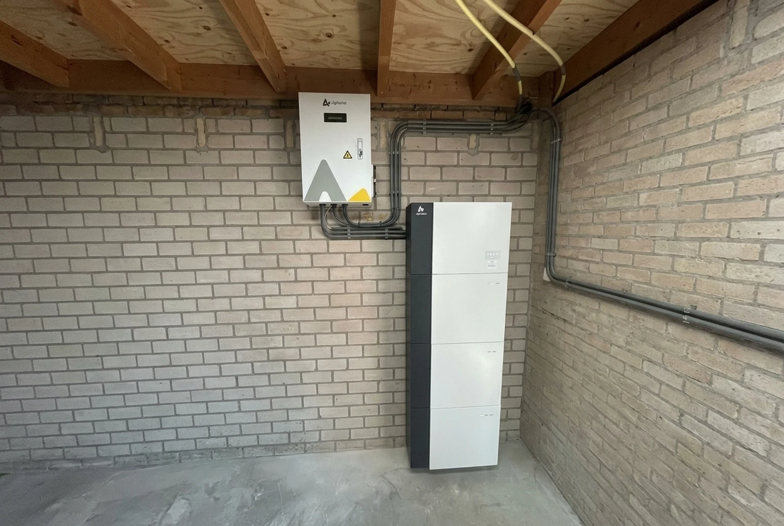 AlphaESS-batterijtoren met omvormerkast en leidingwerk in een ruimte met houten balkenplafond.