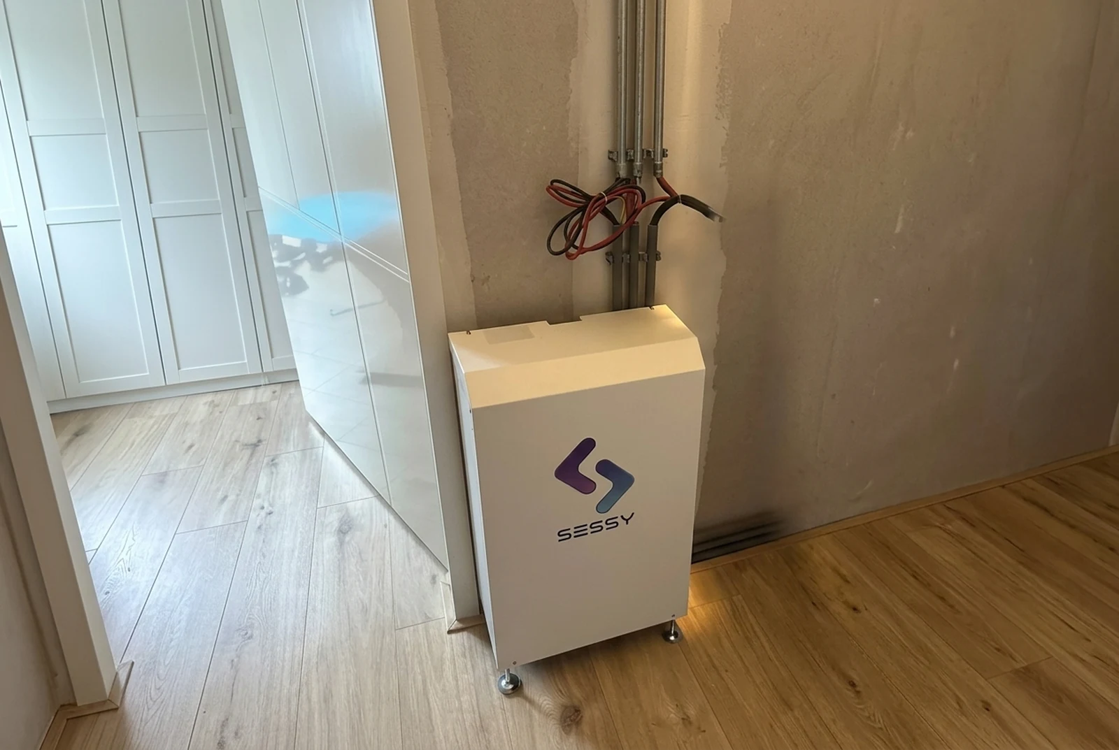 Geïnstalleerde Sessy-thuisbatterij in een Nederlandse woning, op pootjes naast een witte kastenwand.