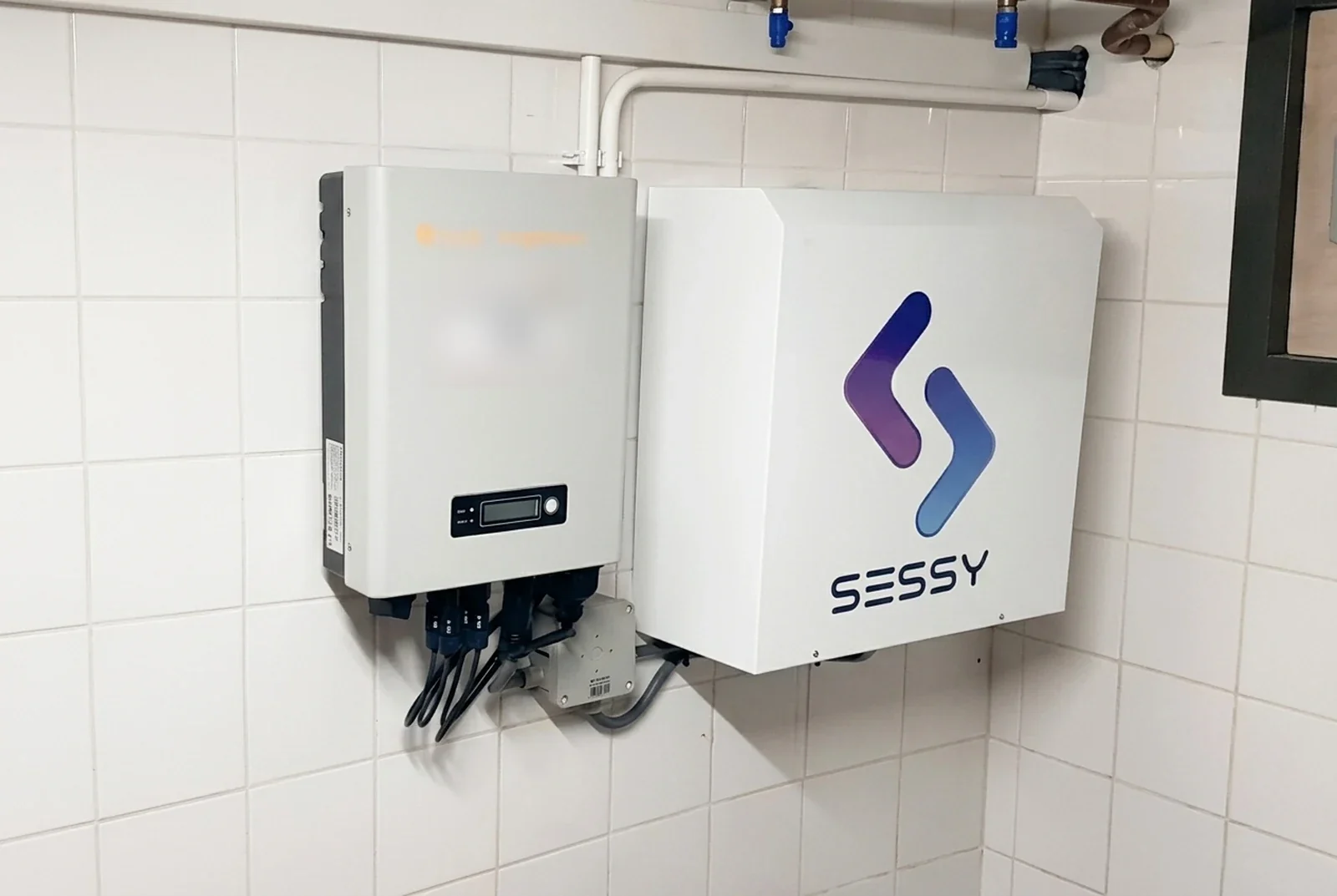 Geïnstalleerde Sessy-thuisbatterij met omvormer aan een betegelde wand.