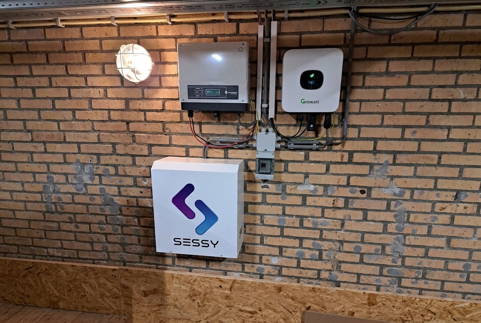 Geïnstalleerde Sessy-thuisbatterij met omvormers op een gele bakstenen muur.